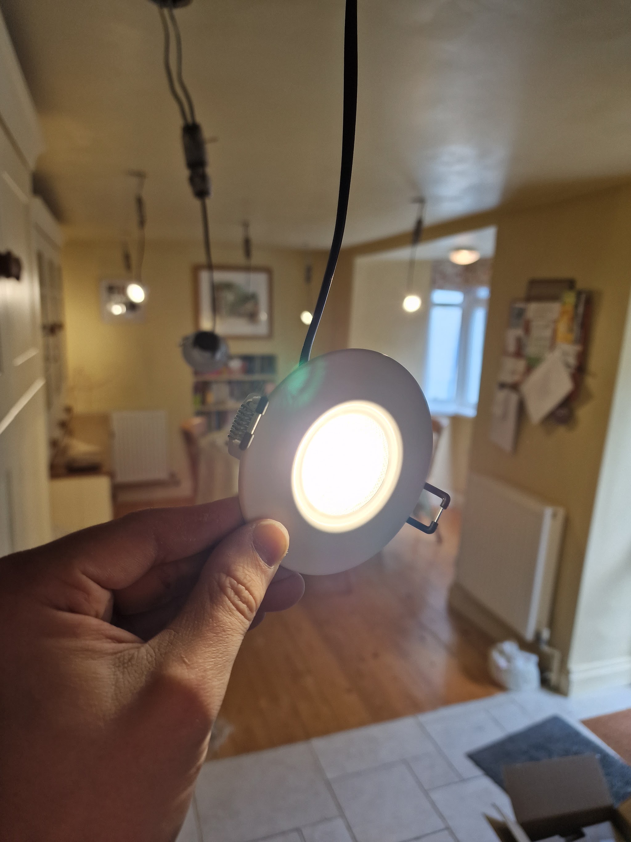 An LED downlight held up, lit, before it goes into the ceiling of a hallway