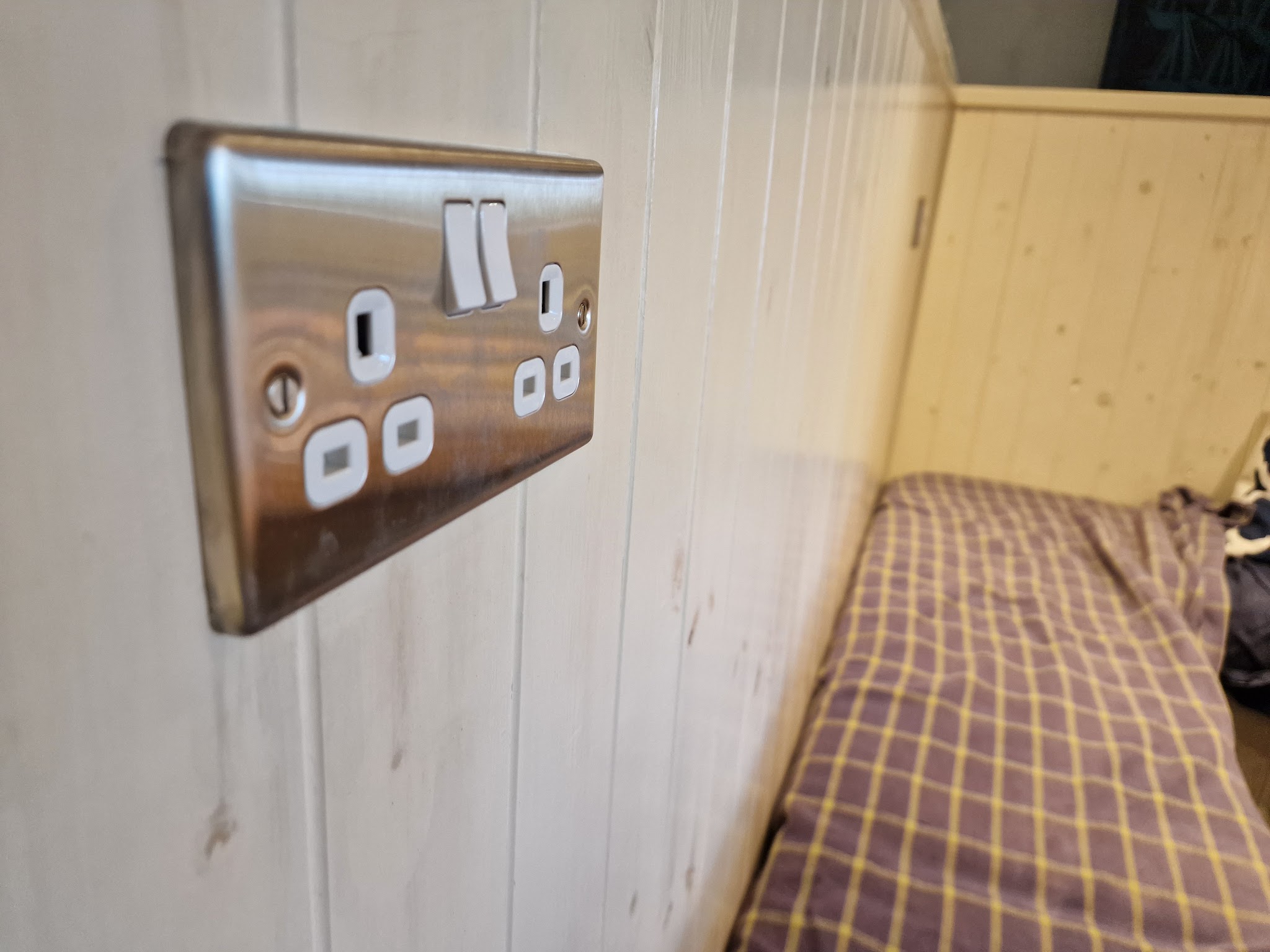 A brushed steel double socket on a timber-clad wall
